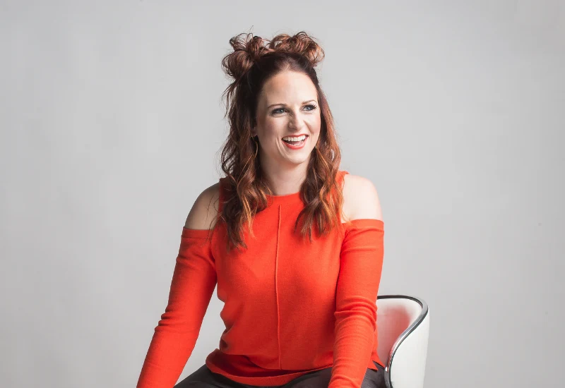 Nicole Roundy seated, smiling, in a red sweater